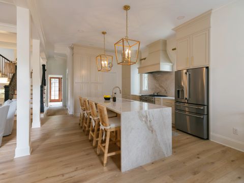 Greenville kitchen with marble waterfall island, cream shaker cabinets, gold fixtures, hardwood floors, and large windows by Tekton Builds.