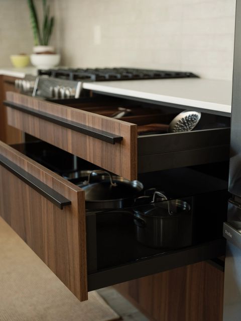 Greenville kitchen with open walnut drawers under gas range storing utensils and stainless cookware, black horizontal pulls, and white countertop by Tekton Builds.