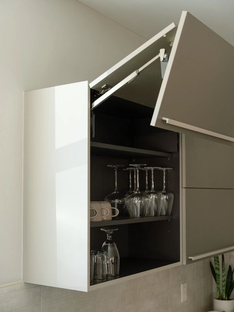 Greenville kitchen with taupe lift-up upper cabinet revealing dark interior shelves with stemware and glassware by Tekton Builds.