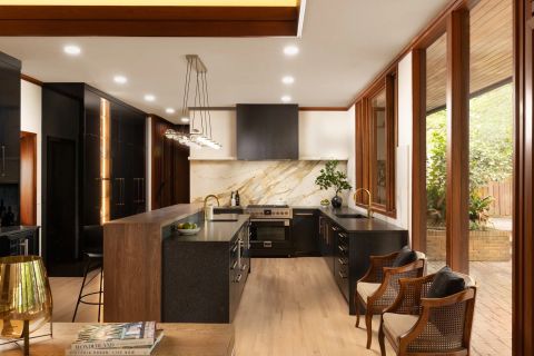 Greenville luxury kitchen with dark cabinetry, warm wood island with waterfall edge, white marble backsplash with gold veining, brass fixtures, and wood-framed windows by Tekton Builds.