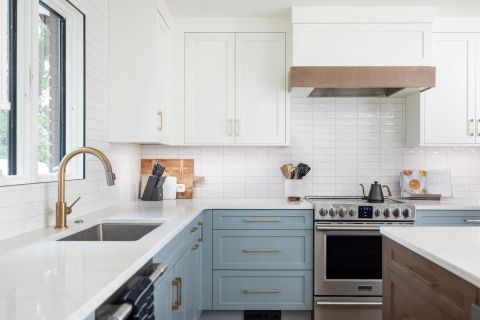 Taylors kitchen with two-tone shaker cabinetry, brushed gold hardware, white countertops, subway tile backsplash, gold gooseneck faucet, and wood-accented range hood by Tekton Builds.