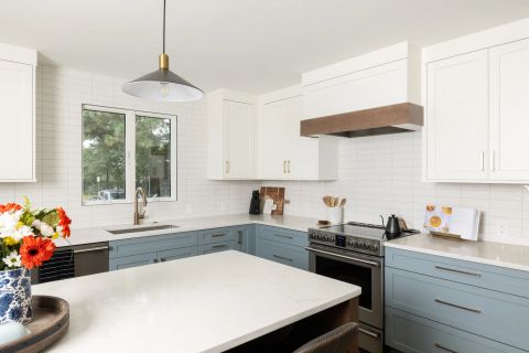 Taylors kitchen with two-tone cabinetry, white uppers, dusty blue lowers, gold bar pulls, white quartz island with dark wood base, and black and gold pendant lights by Tekton Builds.