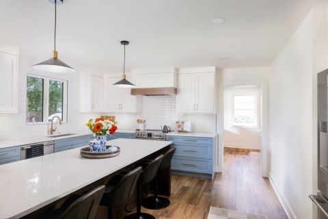 Taylors kitchen with white quartz island with dark wood base, two-tone shaker cabinetry, gold hardware, subway tile backsplash, and stainless steel appliances by Tekton Builds.