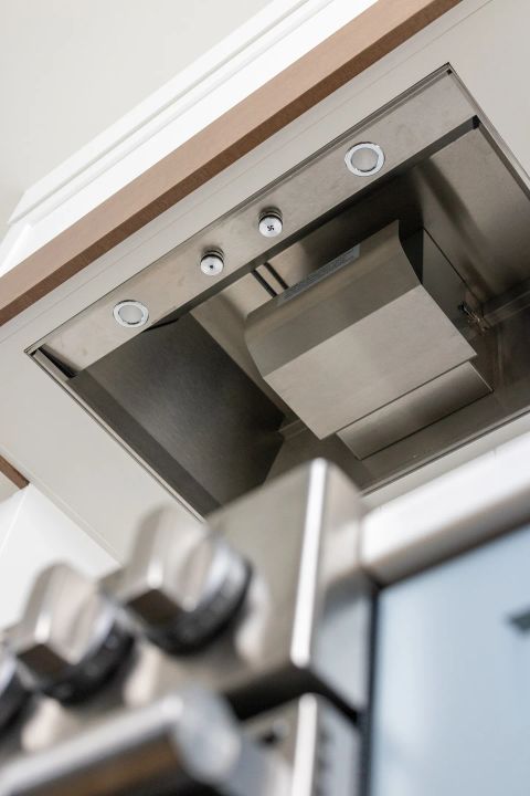 Taylors kitchen with stainless steel range hood, integrated LED lighting, circular control knobs, and white cabinetry with wooden trim by Tekton Builds.