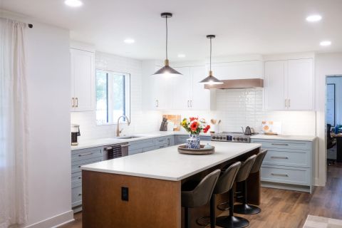 Taylors kitchen with two-tone shaker cabinetry, central island with medium-brown wood base, bar stools, and black metal pendant lights with brass accents by Tekton Builds.