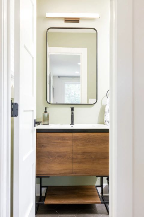 Taylors powder room with dark brown wood-grain vanity, white undermount sink, matte black faucet, rectangular mirror, and sage green walls by Tekton Builds.